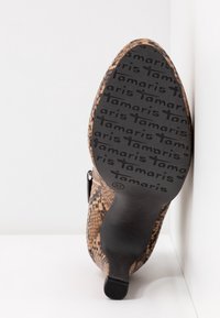 Semelle d'une botte à talon haut marron à motif peau de serpent avec le logo « Tamaris » embossé à plusieurs reprises et la taille 37 indiquée près de la voûte plantaire.