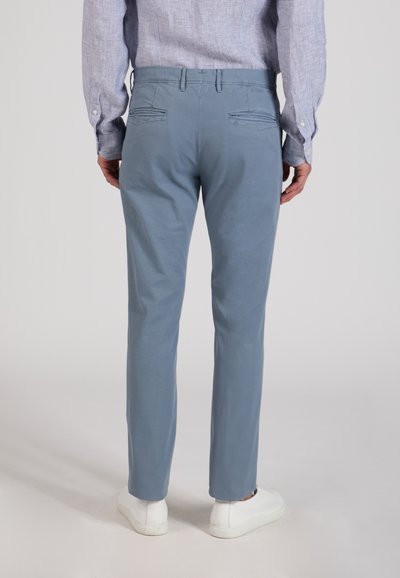 Man wearing light blue slim-fit pants, striped long-sleeve shirt tucked in, and white sneakers, shown from the back.