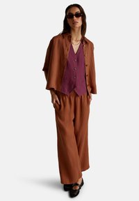 Resavěbarevná lněná bunda přes fialovou vestu, doplněná volnými kalhotami a černými perforovanými botami. Doplňky zahrnují sluneční brýle.