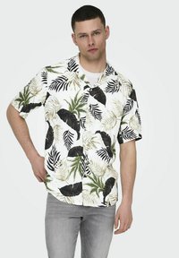 Camisa de manga corta con fondo blanco y grandes patrones de hojas tropicales en verde y negro. Con botones en el frente y un ajuste relajado.
