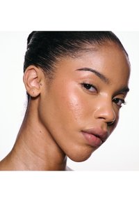 Nærbillede af en kvinde med glat hud, naturlig makeup og hår trukket tilbage, der ser let til siden mod en hvid baggrund.