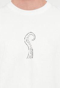 Λευκό μπλουζάκι με μαύρο περίγραμμα ενός πλοκαμιού ξιφία με κυκλικές αναρροφητικές κοιλότητες κοντά στην κορυφή, με λεία υφή, σχεδίαση με στρογγυλή λαιμόκοψη.