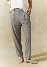 Pantalon à carreaux noir et blanc avec taille haute, plis et poches latérales. Porté avec des ballerines tissées beige clair.