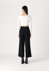 Black wide-leg trousers with an elastic waistband paired with a cropped white long-sleeve top, showcasing a minimalist design and fitted silhouette.