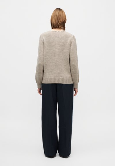 Camisola bege de malha com decote redondo, bainha canelada e mangas compridas, combinada com calças largas azuis-marinho com riscas laterais.