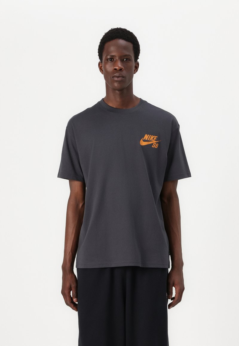 Grå bomulds t-shirt med rund hals, der har et lille orange Nike-logo på venstre bryst. Korte ærmer og afslappet pasform.