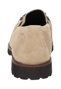 Beige suède schoenen met een ronde neus, een donkere rubberen zool en decoratieve zilverkleurige hardware aan de zijkant. Eenvoudig ontwerp met zichtbare stiksels.