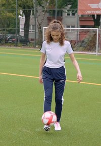 Outfit sportivo Nike, maglietta bianca a maniche corte con accenti neri, pantaloni da track navy con strisce bianche ai lati, e pallone da calcio rosso e bianco su prato verde.