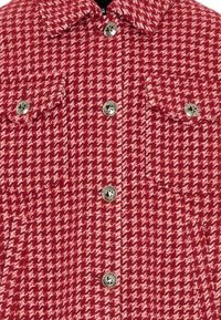 Rood-wit houndstooth-patroon jasje met een kraag, twee voorzakken en metalen knopen. Textiel met een gestructureerd ontwerp.