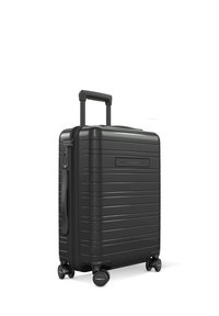 Valise rigide noire avec des rainures verticales, poignée extensible, quatre roues et une serrure latérale. Design compact pour le voyage.