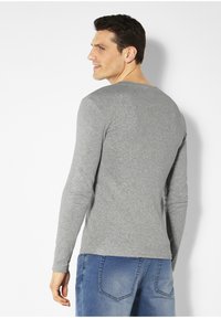Graues langärmeliges Shirt mit rundem Halsausschnitt, aus weichem Baumwollmaterial hergestellt. Verfügt über ein tailliertes Design und dezente Stickdetails.