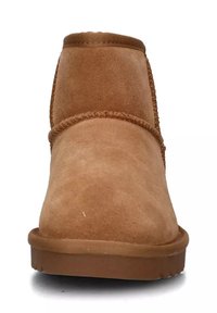 Stivaletto alla caviglia in pelle scamosciata beige con punta tondeggiante, dettagli cuciti lungo le cuciture e suola in gomma piana. Texture morbida, design semplice.