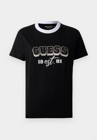 Černé tričko s krátkým rukávem a bílým kulatým výstřihem, na kterém je velkými tučnými písmeny vytištěno "GUESS" a "19 est. 81" na přední straně.