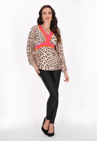 Blouse met een leopardprint patroon, roze accenten bij de halslijn en taille, gecombineerd met zwarte lerenachtige leggings.