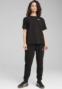 Camiseta de algodón negra y pantalones a juego, con el logo de PUMA, corte relajado y una marca sutil a lo largo del lado de los pantalones. Incluye zapatillas.