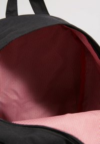 Sac à dos noir avec doublure en tissu rayé vertical rouge et blanc visible à l'intérieur du compartiment principal ouvert.