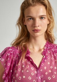 Translucent pink blouse with diamond patterns, frilled short sleeves, and a button-down front. Light texture with a soft, flowy design.