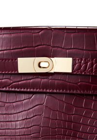 Burgunderröd läderhandväska med krokodiltextur, utrustad med ett guldmetallspänne och sömnadsdetaljer längs kanterna.