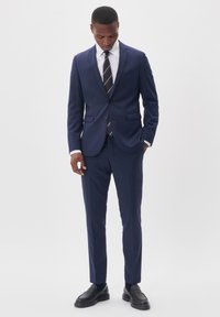 Mörkblå kostym med en skräddarsydd kavaj och matchande byxor, tillverkad av slätt tyg. Komplett med vit skjorta och randigt slips.