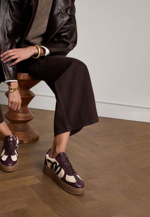 Baskets à plateforme avec une tige en cuir bordeaux et des accents crème, ornées d'une semelle brune texturée, accompagnées de pantalons larges marron.