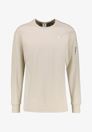 Light beige long-sleeve shirt with textured fabric, ribbed collar and cuffs, featuring a zippered pocket on the left arm.