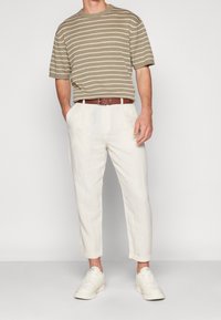 Khakifärgad randig stickad t-shirt kombinerad med ljusa linnebyxor. Ett brunt bälte markerar midjan. Modellen bär vita sneakers.