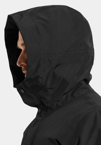 Svart huva jacka med en slät, matt yta, säkrad med tryckknappar, strukturerad huva design och minimalistisk estetik.