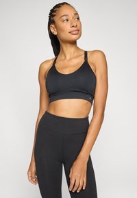 Sort sports-bh med justerbare stropper og glat stof. Har en bred kant forneden. Bæres med sorte leggings i taljen.