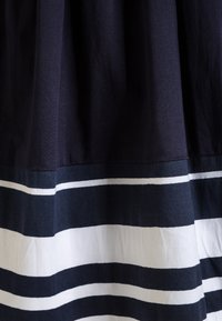 Laikkuva navy-huopa, jossa on kontrastivärinen valkoinen ja sininen vaakaraidoitettu kuosi helman kohdalla, joka omaa sileän tekstuurin ja A-linjaisen muodon.