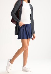 Denim skaterkjol med fransad nederkant, parat med en texturerad vit tröja och en grå cardigan. Buren med vita sneakers och en vinröd väska.