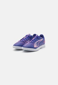 Fioletowe buty sportowe z różowymi akcentami, z teksturowaną siateczką na górze i elastyczną białą podeszwą. Mają smukły design i sznurowanie.