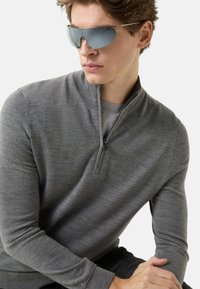 Grauer Langarm-Reißverschluss-Pullover aus strukturiertem Material, kombiniert mit eleganten, spiegelnden Sonnenbrillen. Das Design verfügt über einen hohen Kragen und eng anliegende Ärmel.