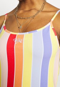 Pestrý pruhovaný top na ramínka v odstínech červené, žluté a fialové. Měkká tkanina s zaobleným výstřihem a vyšitým logem.