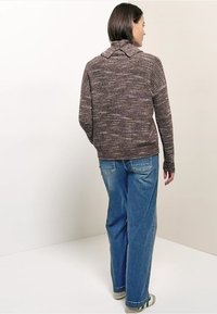 Pull dans des tons violets doux et gris avec un motif tricoté texturé, doté d'une capuche et de manches longues. Associé à un jean bleu clair à jambe droite.
