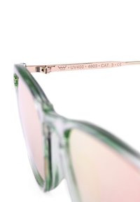 Zelené sluneční brýle ve stylu cat-eye s zrcadlovými skly, kovovými detaily a průhledným rámem. Nabízí UV400 ochranu a rytí značky.