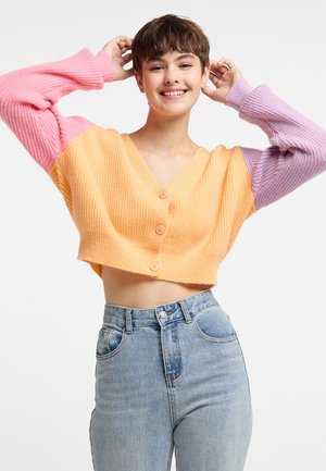 Crochet cropped cardigan dengan tekstur bergaris, menampilkan badan berwarna oranye dan lengan berwarna merah jambu dan ungu, diselesaikan dengan empat kancing di bagian depan.