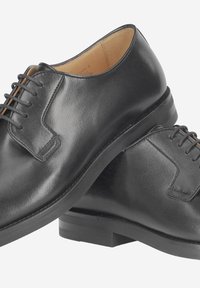 Chaussures en cuir noir à texture lisse, avec un bout arrondi, des lacets apparents et un talon bas et plat. Ornées de coutures minimales.