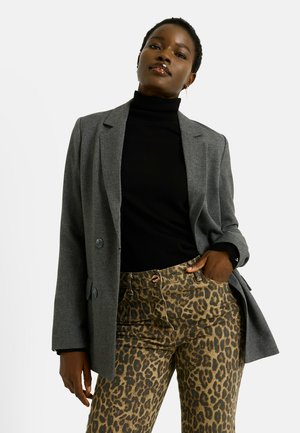 Blazer gris de mezcla de lana con dos botones sobre un cuello alto negro, combinado con pantalones de estampado de leopardo con cierre de botón y cremallera.