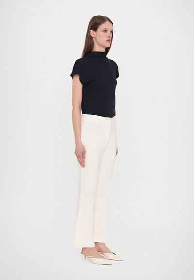 Marineblauw T-shirt met korte mouwen, gecombineerd met witte rechtmatige broek en crèmekleurige muiltjes, met een opstaande kraag en strakke lijnen.