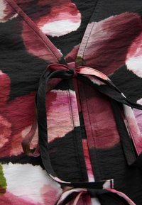 Indumento con motivi floreali e apertura frontale, nei toni del maroon, rosa e verde su uno sfondo nero, caratterizzato da un tessuto morbido e testurizzato.