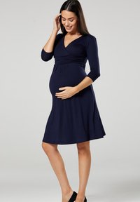 Navy blue maternity dress with three-quarter sleeves, wrap design, and flared skirt. Made from soft fabric, it shows a fitted bodice and waistband.
