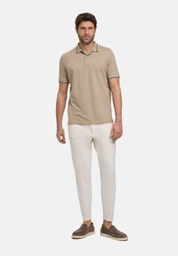 Beige poloshirt met een twee-knopen sluiting en een contrasterende donkere gestreepte kraag, gecombineerd met witte tapered broek en bruine schoenen.