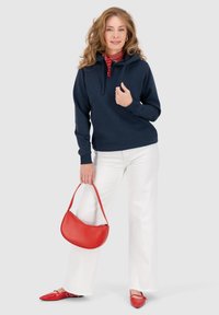 Felpa blu marina, pantaloni bianchi a gamba larga, borsa rossa e scarpe rosse. Una notable sciarpa rossa a pois accompagna l'outfit.