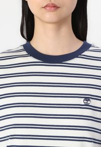 Stripped cotton t-shirt featuring navy and white horizontal stripes, ribbed navy crew neck, and a small embroidered logo on the chest.