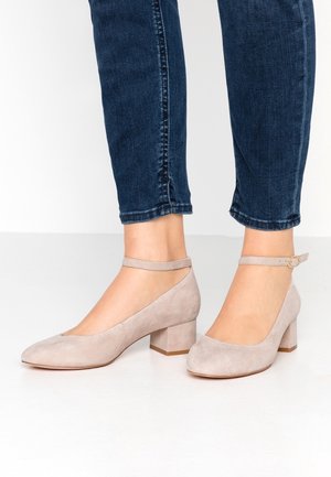 Beige Wildleder-Blockabsatzschuhe mit einer runden Zehenpartie und einem Knöchelriemchen, kombiniert mit dunkelblauen engen Jeans. Glatte Textur, minimalistisches Design.