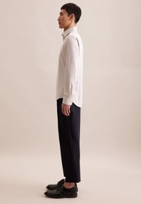 Lichtgrijze overhemd met lange mouwen en een kraag, gecombineerd met marineblauwe broek en zwarte schoenen. Glad materiaal met een eenvoudig, op maat gemaakt ontwerp.