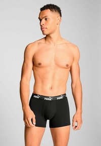 Black boxer shorts made of cotton, featuring an elastic waistband with white "PUMA" branding. Simple, fitted design with a mid-rise cut.