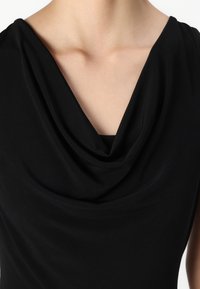 Sorte ermeløs topp med drapert cowl-halslinje, glatt tekstur og tettsittende design som fremhever skuldrene og kragebeinet.