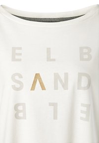 Bijela pamučna majica s raspršenim svijetlosivim tekstom, s riječju "SAND" u tamnijoj nijansi. Okrugli izrez s teksturiranim unutarnjim ovratnikom.