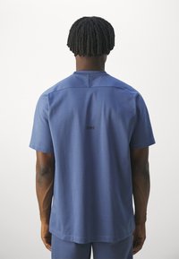 Granatowa koszulka z krótkim rękawem, okrągłym dekoltem, gładką teksturą i logo nadrukowanym na plecach. Prosty, nowoczesny design. Gładkie tło.